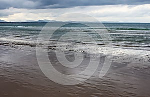 Wet beach as the tide recedes with blue mountains ranges in the distance under a stormy sky - Byron Bay NSW Australia