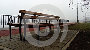 Wet bench on a foggy day. Metal curled wrought iron fence detail. Off-season melancholic mood