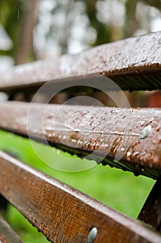 Wet bench in the park in the rain. Rainy weather. Wooden chair in the rain. Wet urban furniture. Rain drops on wooden