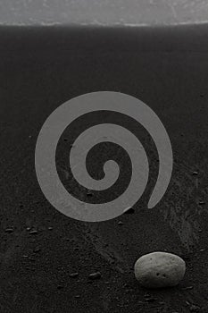 Wet black volcanic sand on shore with white stone, zen, texture, background, vertical.