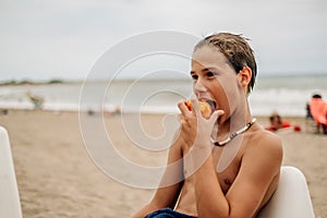 Wet boy biting apricot on the beach