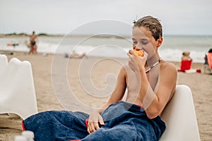 Wet boy eating peach on the beach