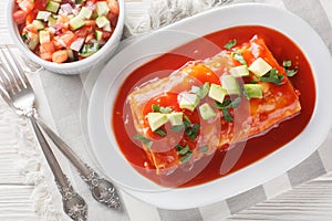 Wet burrito recipe made with flour tortillas filled with ground beef, refried beans, and chiles closeup on the plate. Horizontal