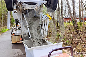 Wet cement coming down cement truck chute into a wheelbarrow track concrete buggy at a construction site