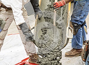 Wet cement off loaded by construction workers using a shovel from a cement truck chute into a concrete form