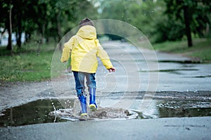 A wet child is jumping in a puddle. Fun on the street. Tempering in summer