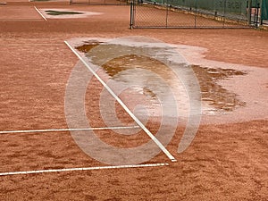 Wet clay tennis court with puddles during the rain.