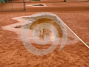 Wet clay tennis court with puddles during the rain.