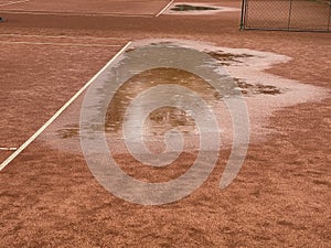 Wet clay tennis court with puddles during the rain.