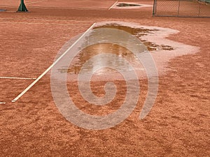 Wet clay tennis court with puddles during the rain.