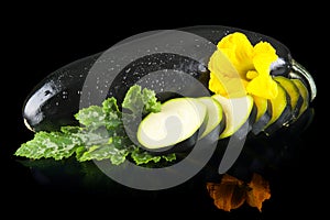 Wet courgettes cut into slices with flower and leaf on black