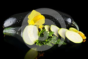 Wet courgettes cut into slices with flower and leaf on black