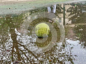 Wet dirty tennis ball in puddle in rainy weather. Cancellation of matches.