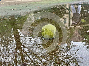 Wet dirty tennis ball in puddle in rainy weather. Cancellation of matches.