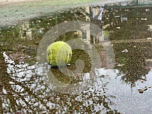 Wet dirty tennis ball in puddle in rainy weather. Cancellation of matches.