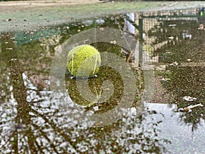 Wet dirty tennis ball in puddle in rainy weather. Cancellation of matches. Water reflection