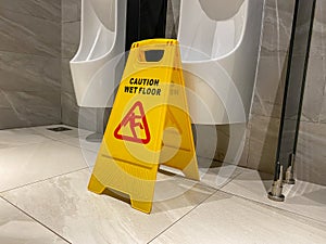 Wet floor caution sign in male toilet room near the urinals