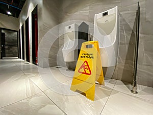 Wet floor caution sign in public male restroom near urinals area