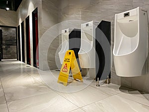 Wet floor sign near urinals area in public toilet during cleaning process