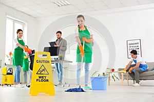 WET FLOOR sign and team of professional janitors