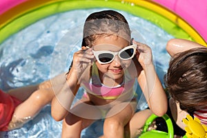 A wet girl in sunglasses is sitting in a small inflatable pool
