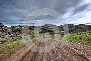 Wet gravel road winding through grass covered hills under stormy sky