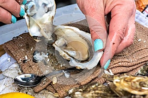 Wet hands of a girl with painted nails opening an oyster