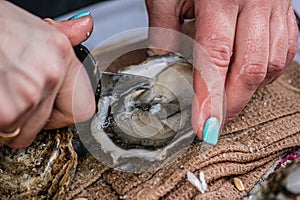 Wet hands of a girl with painted nails opening an oyster with a small knife