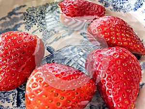 Wet juicy luscious strawberries shiny on blue white dutch plate close up