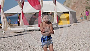 wet little boy in blue shorts freeze and shiver shake on summer beach after swimming during holiday vacation travel to