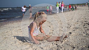 Wet little girl put sand on her legs sitting on coastline of Baltic sea