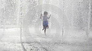 Wet little girl running and having fun in the jet fountain at city public park.