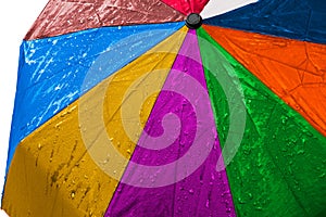 Wet multicolored umbrella close up image on isolated background. Waterproof fabric cloth with water drops and splashes. Rainbow