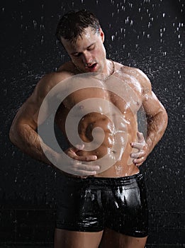 Wet muscle young man posing under the rain