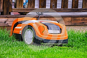 Wet orange automatic lawn robot mower at charging station, close to wooden terrace