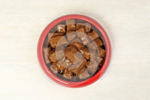 Wet pet food in feeding bowl on white table, top view