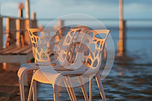 Wet plastic chairs after the rain on the shore illuminated by the sunset light