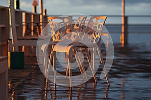 Wet plastic chairs after the rain on the shore illuminated by the sunset light