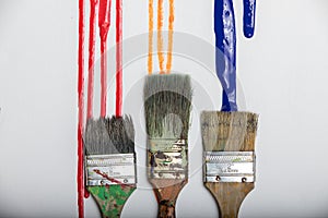 Wet paint dripping down onto three clean paintbrushes on white canvas background