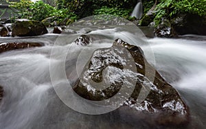 Wet rock in the middle of clear water flowing river surrounded by rapids and stream