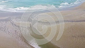 Wet sand on the beach and tidal sea waves, top view. Sandy beach and white foam on the ocean surface, drone video. Seascape