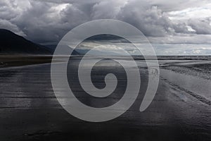 Wet sand reflects the clouds from a stormy sky along the coast