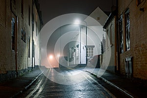 A wet street with historic buildings with street lights glowing on a misty winters night. Upton Upon Severn, UK