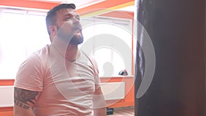 Wet and sweaty, bearded caucasian man boxing a punching bag in training at the gym