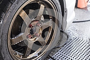 A wet tire and rim of a sedan still with soap suds after a through cleaning. At a carwash