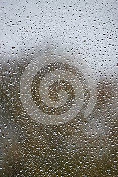 Wet with water drops glass window with light grey rainy background, closeup