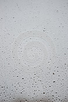 Wet with water drops glass window with light grey rainy background, closeup