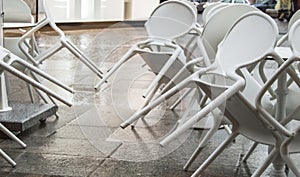 Wet white plastic chairs with raindrops in a street cafe, overturned, after a rain in Italy, in the evening