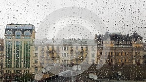 Wet window with drops on the background of the autumn city in cloudy weather. View from the window in the rain. Water drop on