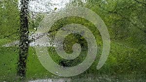 Wet window glass with rain drops with green  trees and grass outside